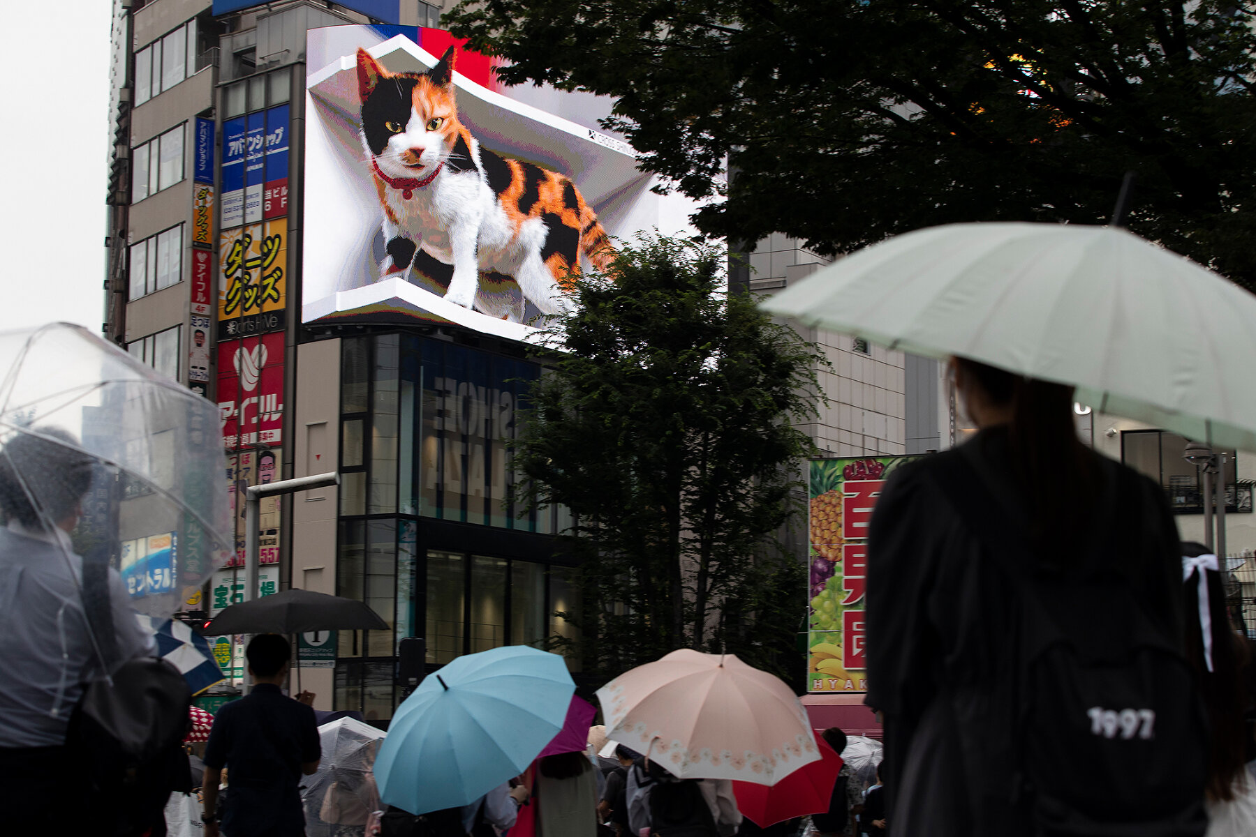<p>Прохожие рассматривают огромную 3-D рекламу, установленную незадолго до Игр на одном из зданий торгового квартала Синдзюку в Токио, 9 июля 2021 года</p>
