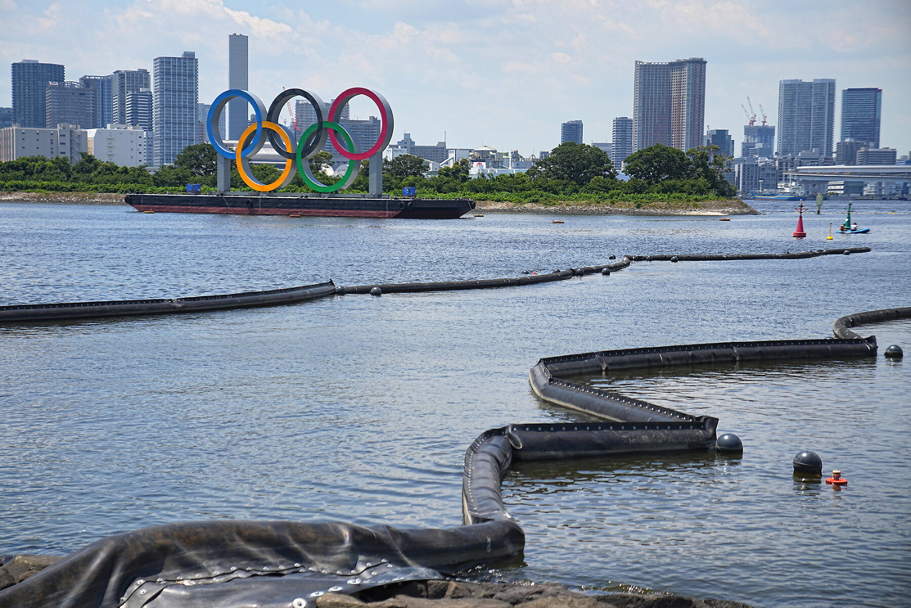 <p>Вид на залив Одайба в Токио с понтоном, на котором установлены олимпийские кольца, 20 июля 2021 года. На переднем плане видны плавучие фильтры, которые должны уменьшать уровень загрязнения воды в заливе</p>